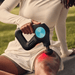 Seated female using Theragun PRO Plus massage gun with infra red light to massage quads
