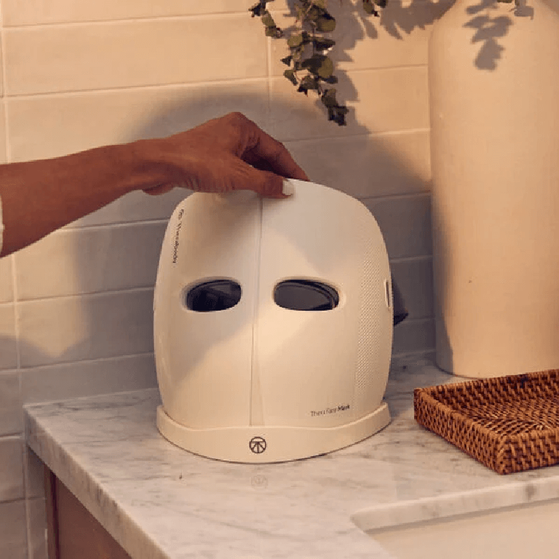 White Theraface Mask sitting on charging station on marble bench